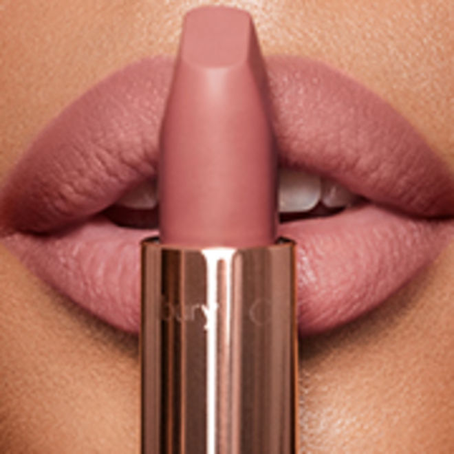 Matte Revolution in Pillow Talk Original on medium-tone model lips close-up Lips close-up of a model wearing a matte, nude pink lipstick while holding the lipstick in front of her lips.