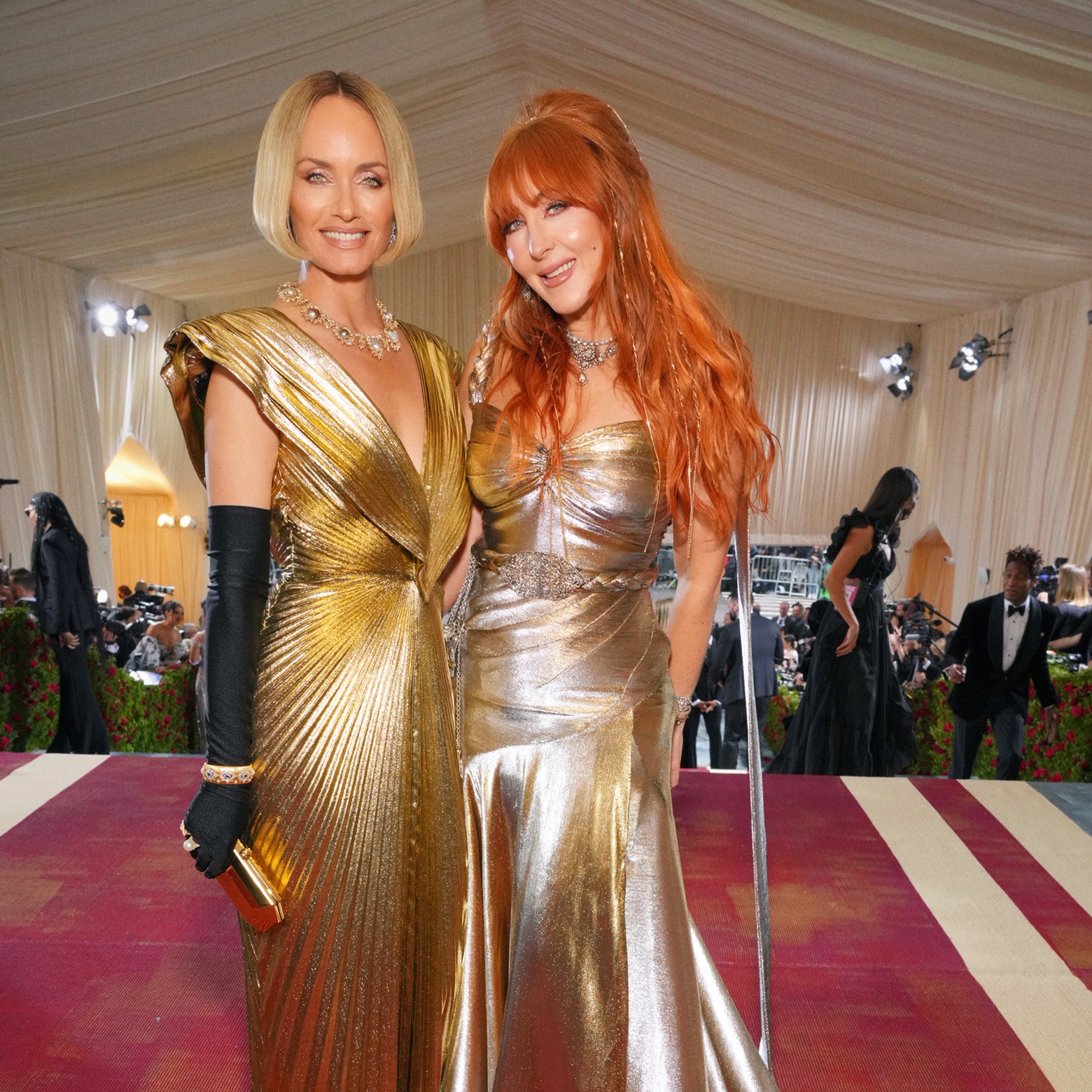 Charlotte Tilbury with a model on The Met Gala, both wearing shiny, reflective gowns in silver and gold with full-glam nude pink makeup.