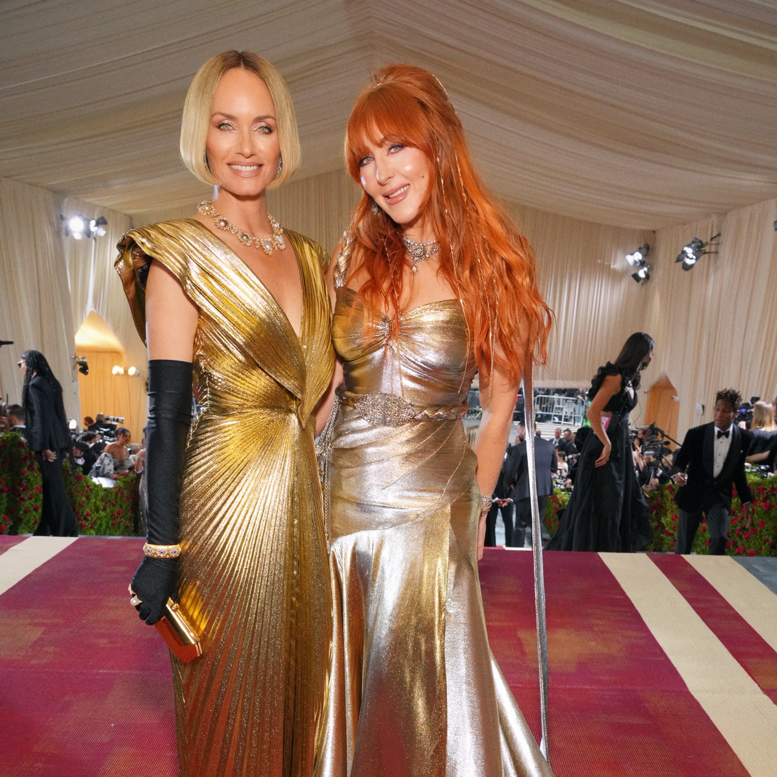 Charlotte Tilbury with a model on The Met Gala, both wearing shiny, reflective gowns in silver and gold with full-glam nude pink makeup.