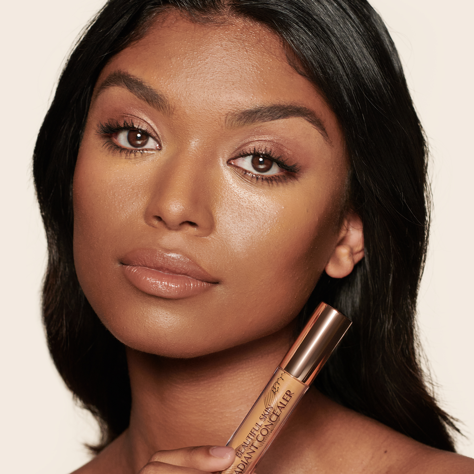 Deep-tone model with brown eyes wearing a radiant, concealer that brightens, covers blemishes, and makes her skin look fresh along with nude lip gloss and subtle eye makeup.