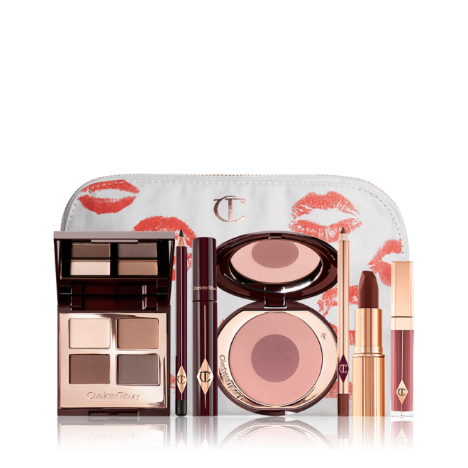 A white makeup pouch with a quad eyeshadow palette in shades of champagne, gold, and bronze, a dark brown eyeliner pencil, mascara, a two-tone brown and pink powder blush, tawny-brown lip liner, a maroon lipstick, and a warm pinkish-red lip gloss. 