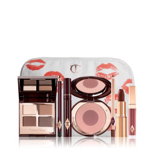 A white makeup pouch with a quad eyeshadow palette in shades of champagne, gold, and bronze, a dark brown eyeliner pencil, mascara, a two-tone brown and pink powder blush, tawny-brown lip liner, a maroon lipstick, and a warm pinkish-red lip gloss. 