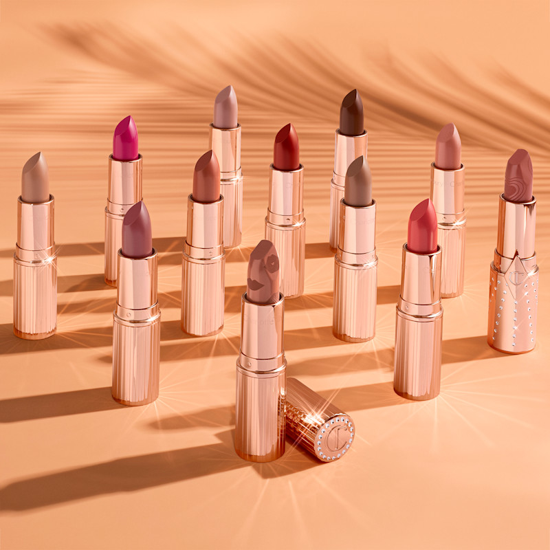 A collection of satin lipsticks in gold-coloured tubes in shades of peach, magenta, coral, brown, red, and nude pink. 
