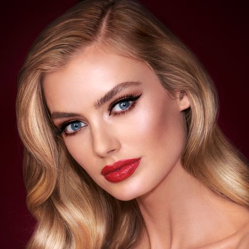 A light-tone model with blue eyes wearing shimmery bronze eye makeup with muted pink blush and glossy scarlet-red lips