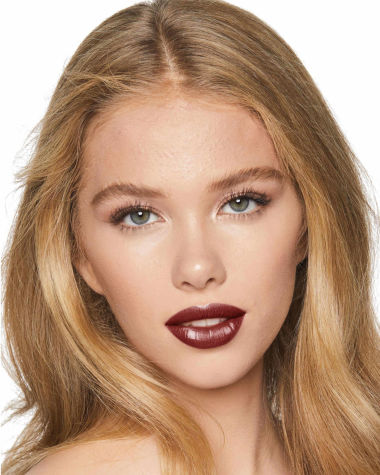 Fair-tone model with grey eyes wearing a moisturising lipstick balm in a berry shade with a high-shine finish.