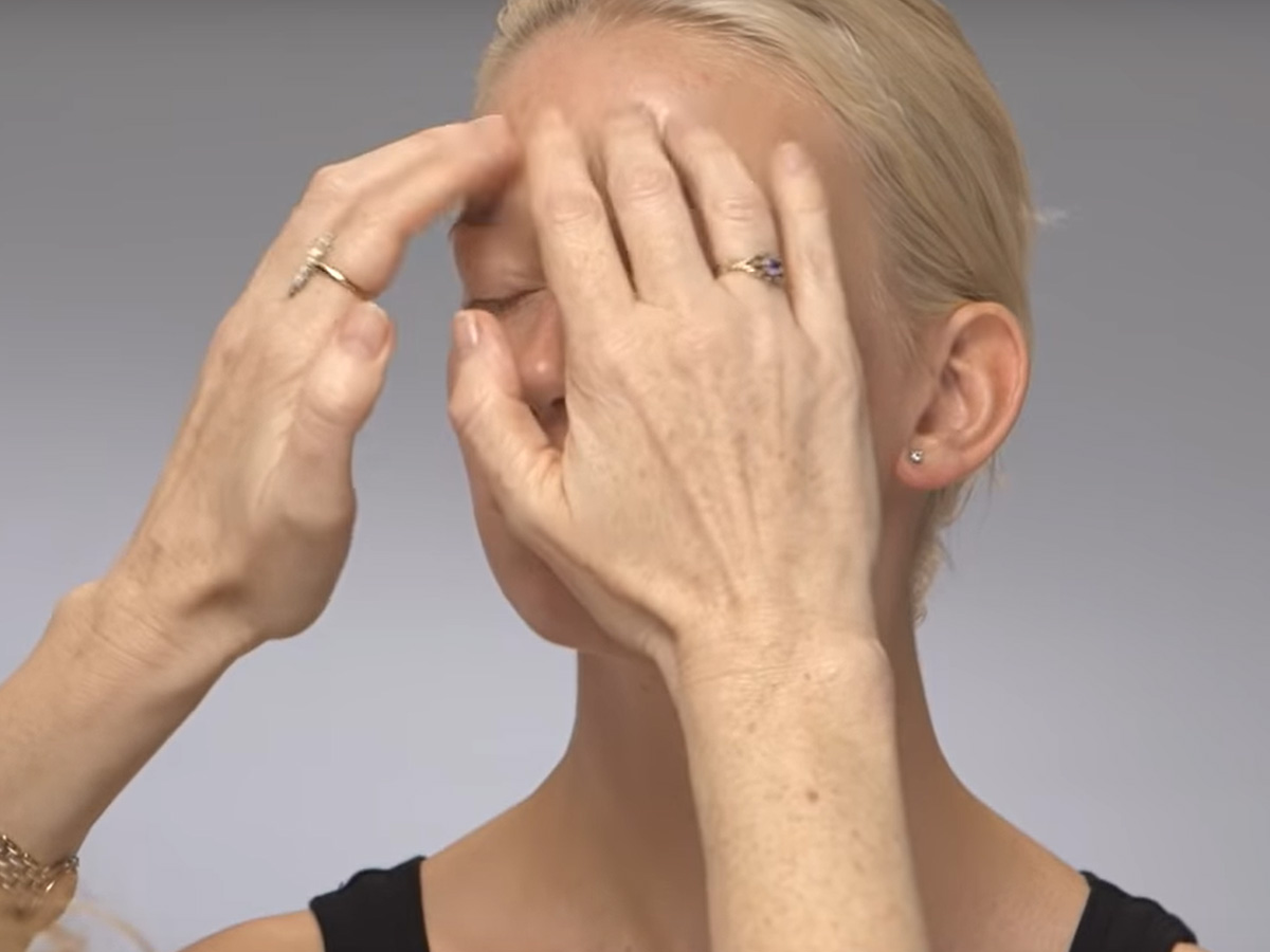 A light-tone blonde model getting a dewy face cream massaged on her forehead. 