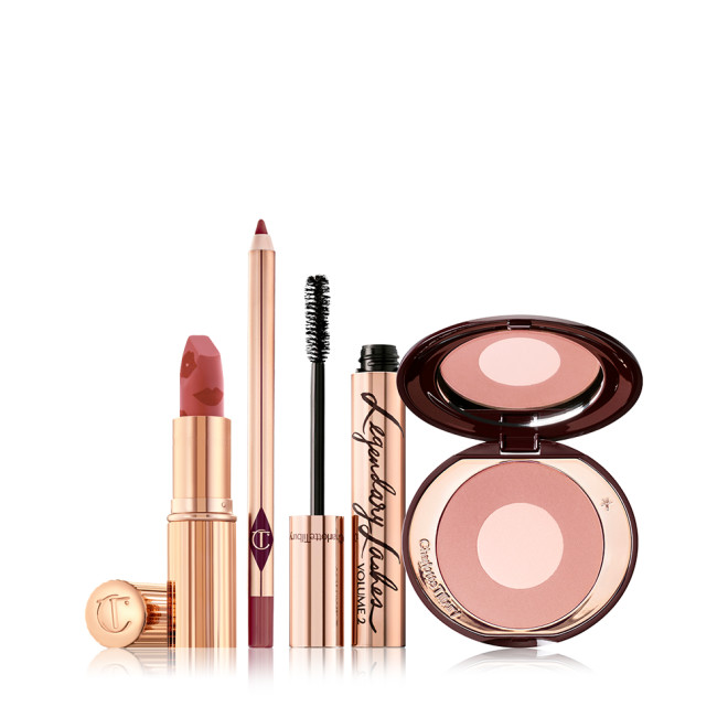 An open matte lipstick in warm pink with a warm-pink lip liner pencil, black mascara in gold packaging, and two-tone blush in a nude pink shade. 