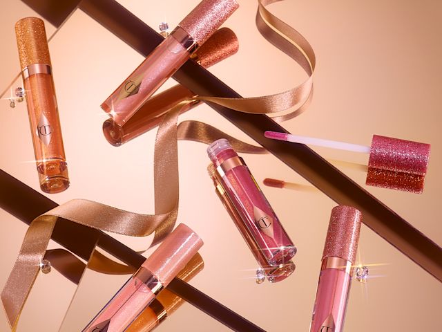 A collection of shimmery lip glosses in shades of pink, gold, and champagne in glass tubes with glittery lids. 