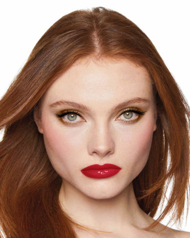 A fair-tone model with grey eyes wearing shimmery bronze eye makeup with muted pink blush and glossy scarlet-red lips