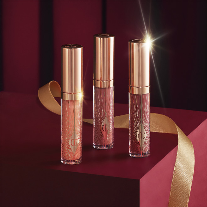 Three lip glosses in shades of light pink, coral-peach, and brown-pink in glass tubes with gold-coloured lids. 