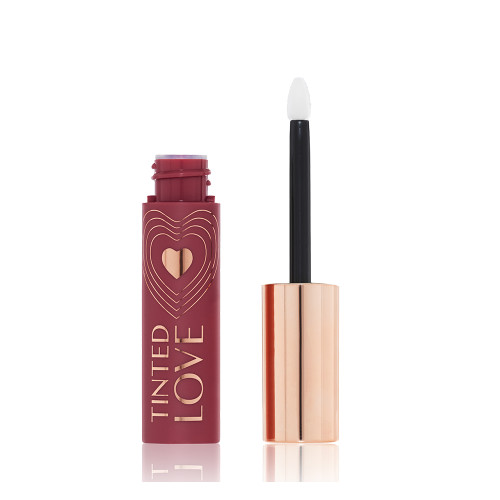 An open lip and cheek tint with a gold-coloured lid in a dark cherry-red-coloured tube.