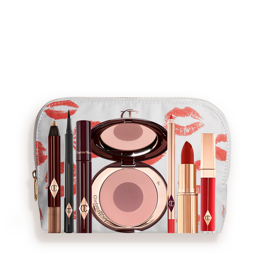 A white makeup pouch with an open two-tone blush in cool-toned pink and brown with a mascara, eyeliner pen, chubby eyeshadow stick in gold, an open lipstick in bold red, lip liner pencil in blood-red, and a lip gloss in bright red. 