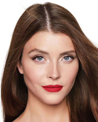 A fair-tone model with blue eyes wearing a matte, bright, cherry-red lipstick.