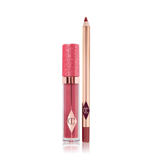 Shimmery lip gloss in a berry-pink shade in a glass tube with a glittery lid with an open lip liner pencil in a dark berry-pink shade. 