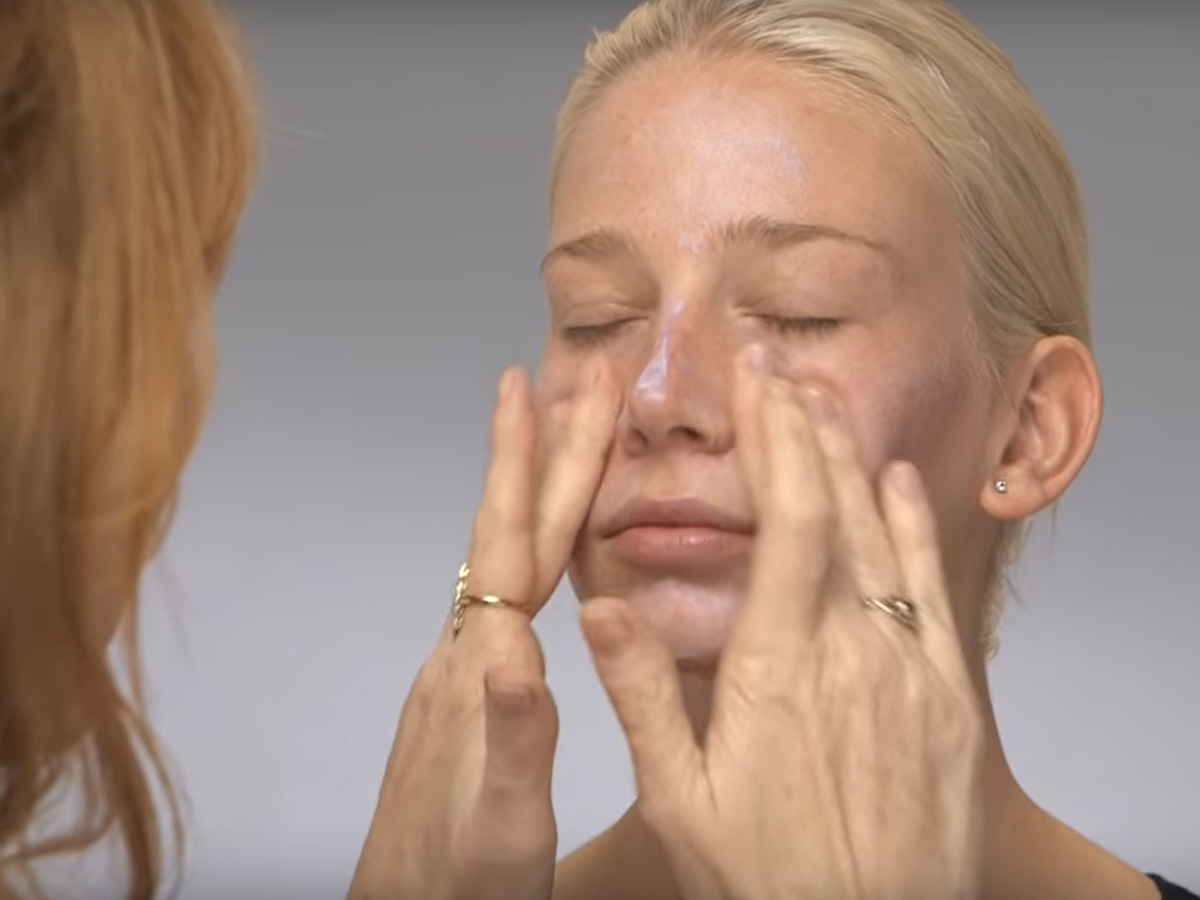 A light tone, blonde model getting a dewy, face cream with a luminous finish applied on her cheeks.
