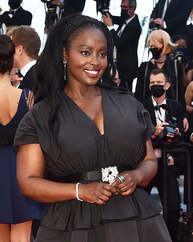 Aissa Maiga at Cannes Film Festival 2021, wearing smokey eye makeup with a bold red lip and a black dress with a low-cut neckline.