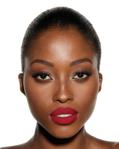A deep-tone model with brown eyes wearing a matte, bright, cherry-red lipstick.
