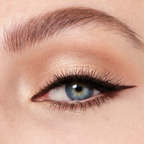 Single-eye close-up of a fair-tone model with blue eyes wearing smokey champagne and brown eye makeup with black eyeliner in a thick wing and nude eyeliner on her lower waterline.