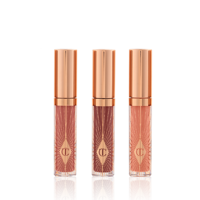 Three, travel-size lip glosses in shades of light pink, coral-peach, and brown-pink in glass tubes with gold-coloured lids. 