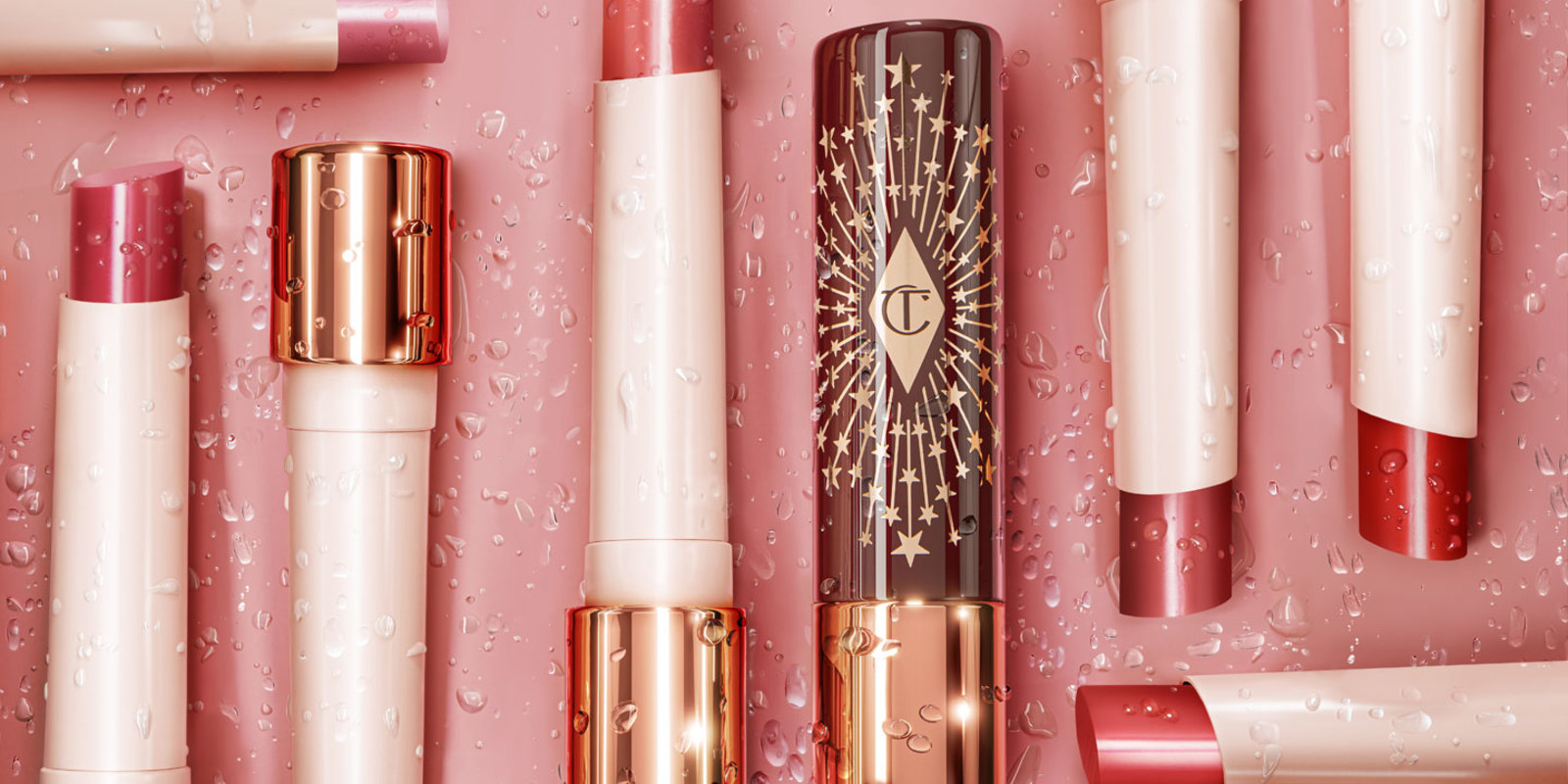 A collection of open, moisturising, high-shine lipstick balms in shades of red, pink, purple, brown, peach, and coral in white and gold-coloured tubes with black-coloured lids with gold-coloured stars printed all over.