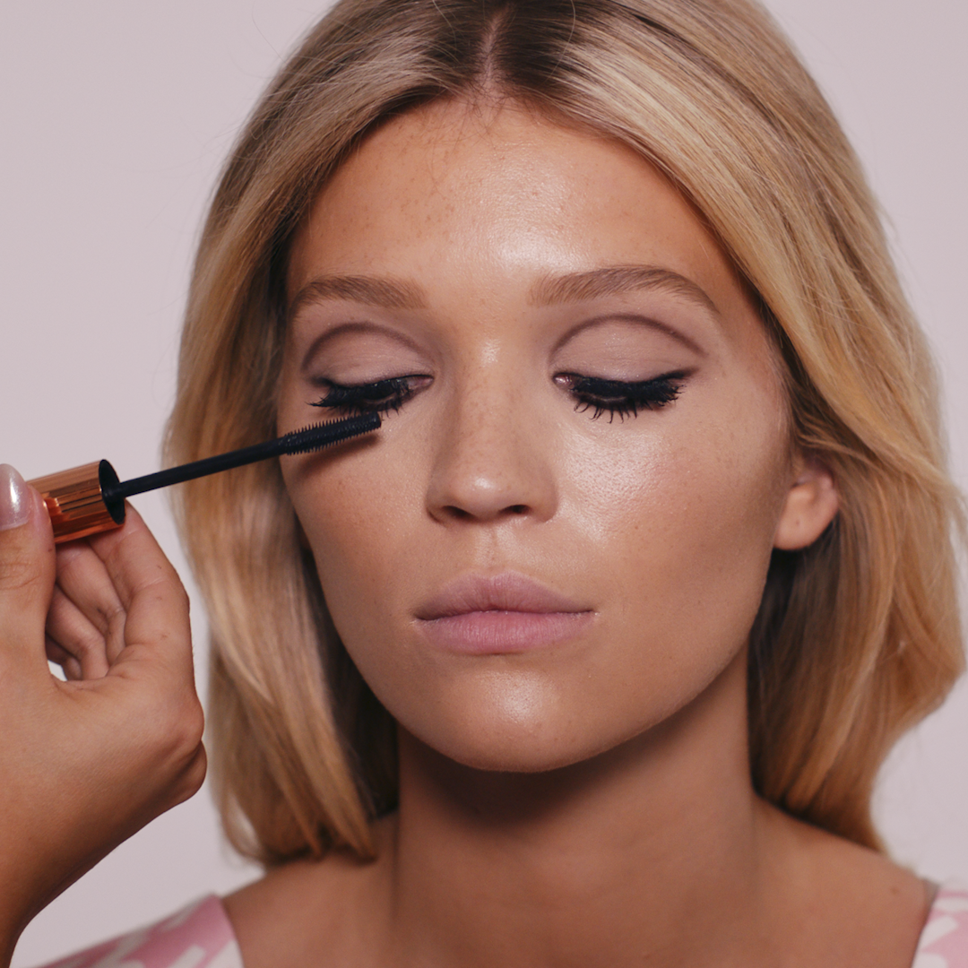 Makeup artist applying mascara to lashes of fair blonde model, creating a 60s makeup look.