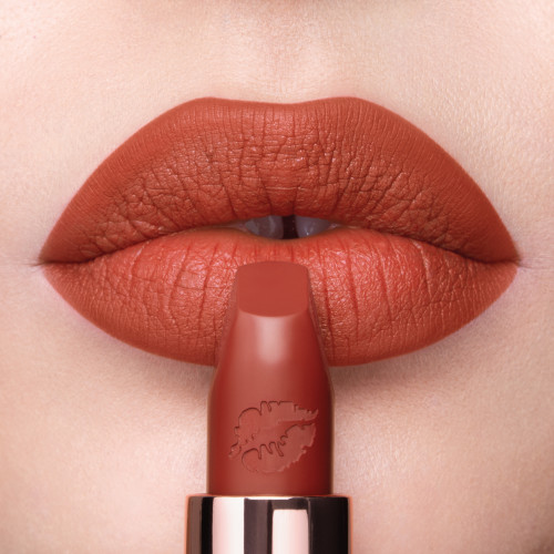 Lips close-up of a fair-tone model wearing a matte, burnt-orange red lipstick.