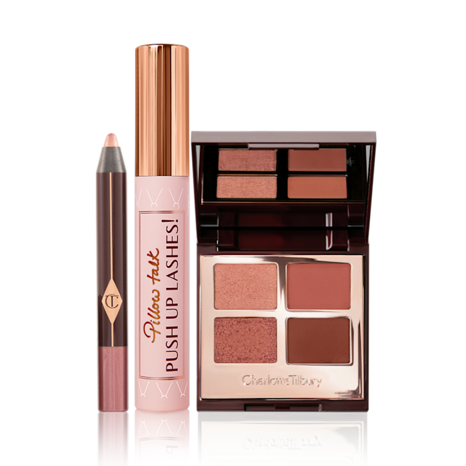 Pillow Talk Party Eyes Kit open An eyeshadow stick in nude pink, black mascara in nude pink tube with a gold-coloured lid, an open quad eyeshadow palette in shades of brown with a mirrored lid.