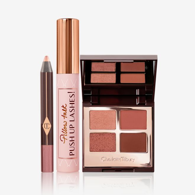 Pillow Talk Party Eyes Kit open An eyeshadow stick in nude pink, black mascara in nude pink tube with a gold-coloured lid, an open quad eyeshadow palette in shades of brown with a mirrored lid.