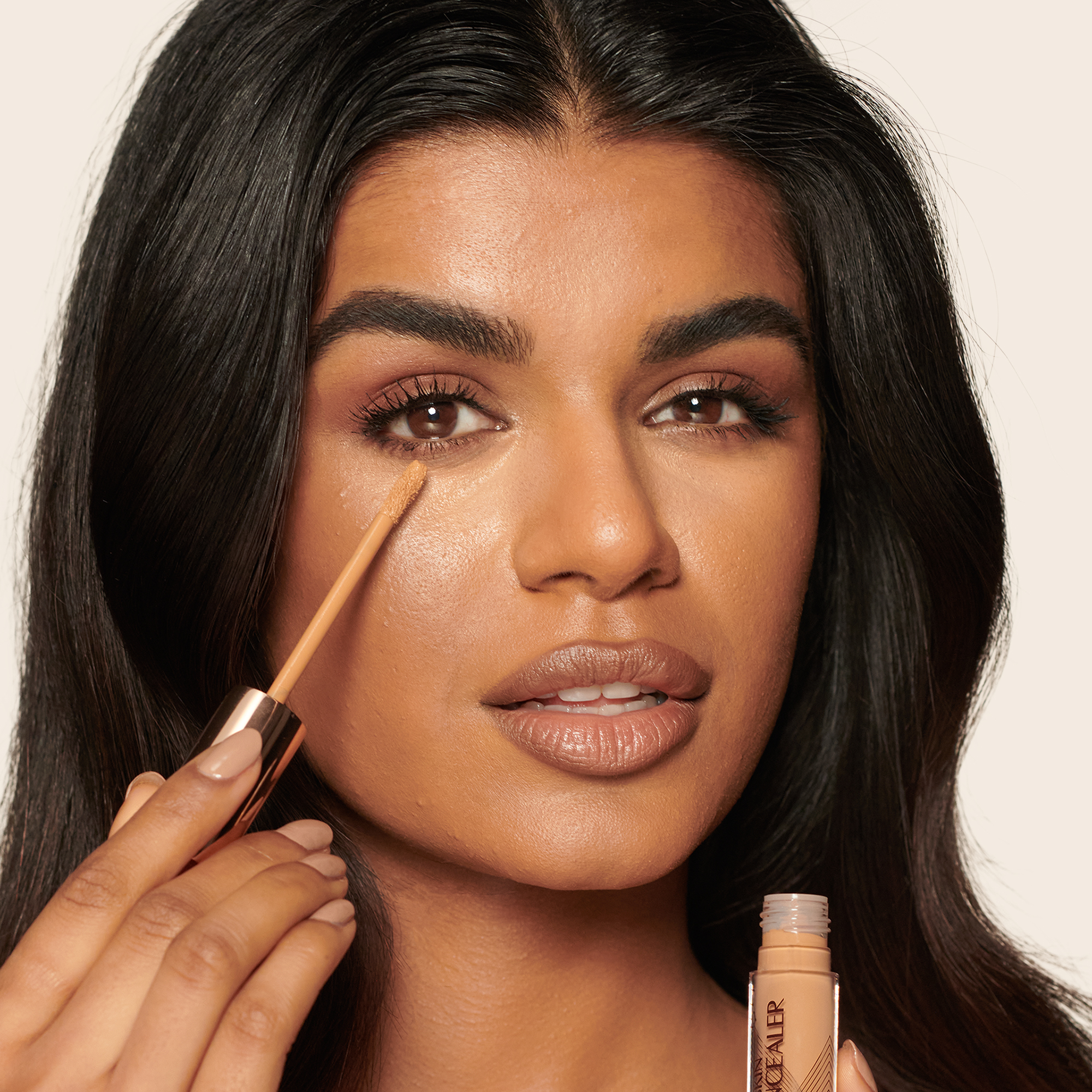 Deep-tone model with brown eyes wearing a radiant, concealer that brightens, covers blemishes, and makes her skin look fresh along with nude lip gloss and subtle eye makeup.