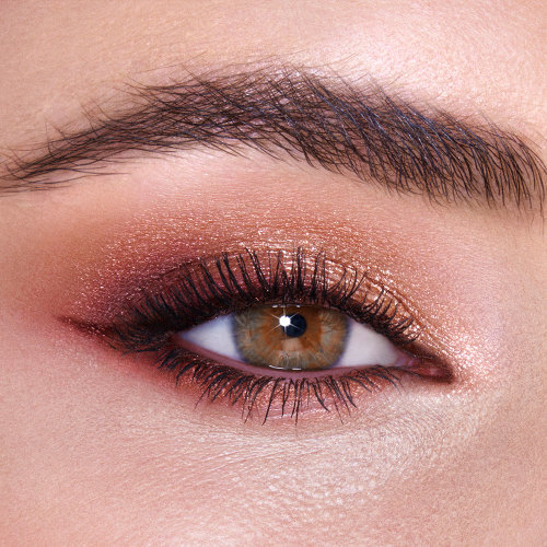 Single-eye close-up of a fair-tone model with hazel eyes wearing shimmery rose gold and smokey brown eye shadow. 