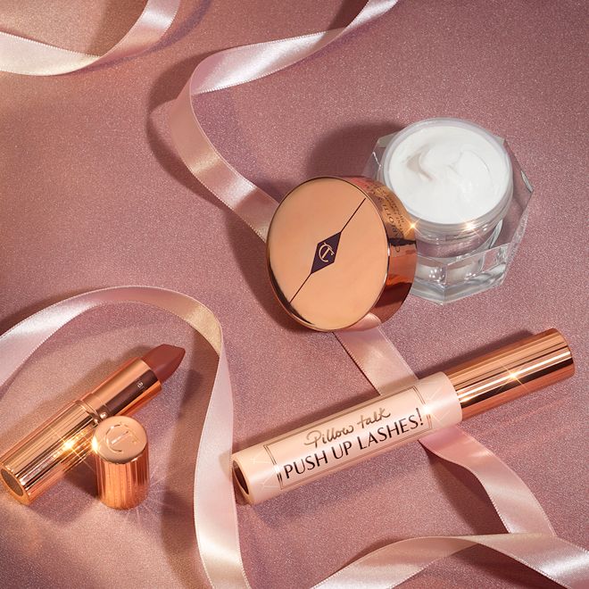 Charlotte Tilbury's Magic Icons kit displayed Pearly-white face cream in an open glass jar with a gold-coloured lid, black mascara in a pink tube with a gold-coloured lid, and golden-peach matte lipstick in a gold-coloured tube.