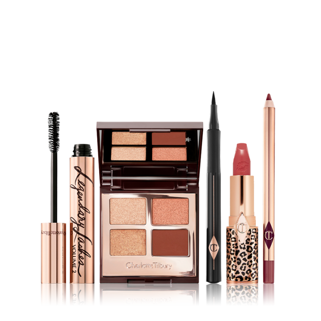 An open mascara tube with its applicator next to it, an open, mirrored-lid quad eyeshadow palette with matte and shimmery brown and golden shades, an open eyeliner pen, a matte lipstick in terracotta-red with a matching lip liner pencil.