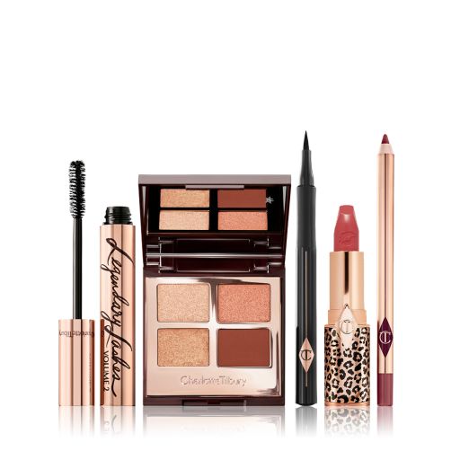 An open mascara tube with its applicator next to it, an open, mirrored-lid quad eyeshadow palette with matte and shimmery brown and golden shades, an open eyeliner pen, a matte lipstick in terracotta-red with a matching lip liner pencil.