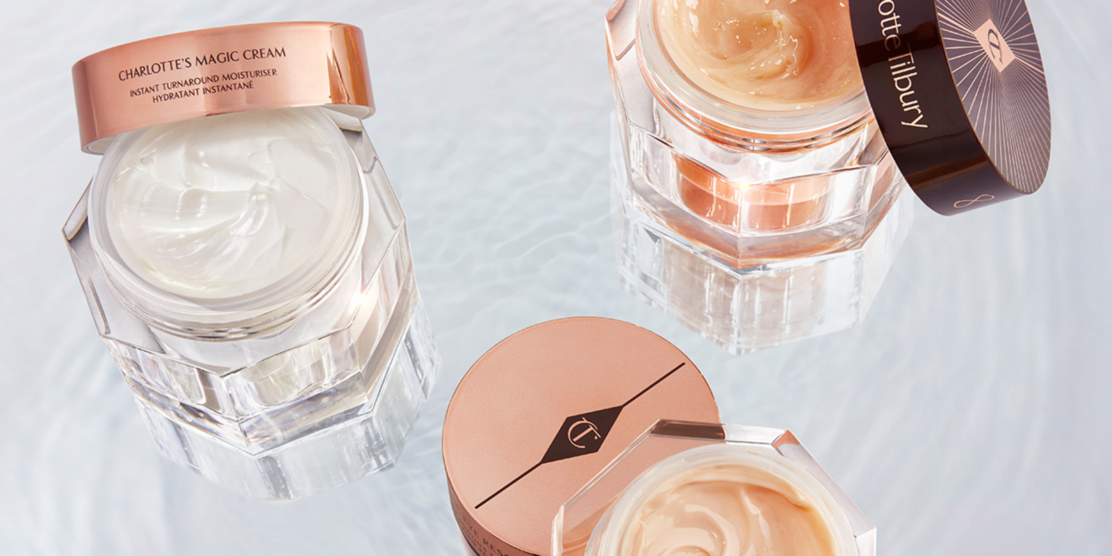 A collection of skincare that includes a textured-cloth face mask, an open, luminous ivory-coloured serum in a glass bottle, lip oil tubes, eye, day, and night creams in glass jars with gold-coloured lids, and primer in a white tube with a white-coloured lid.