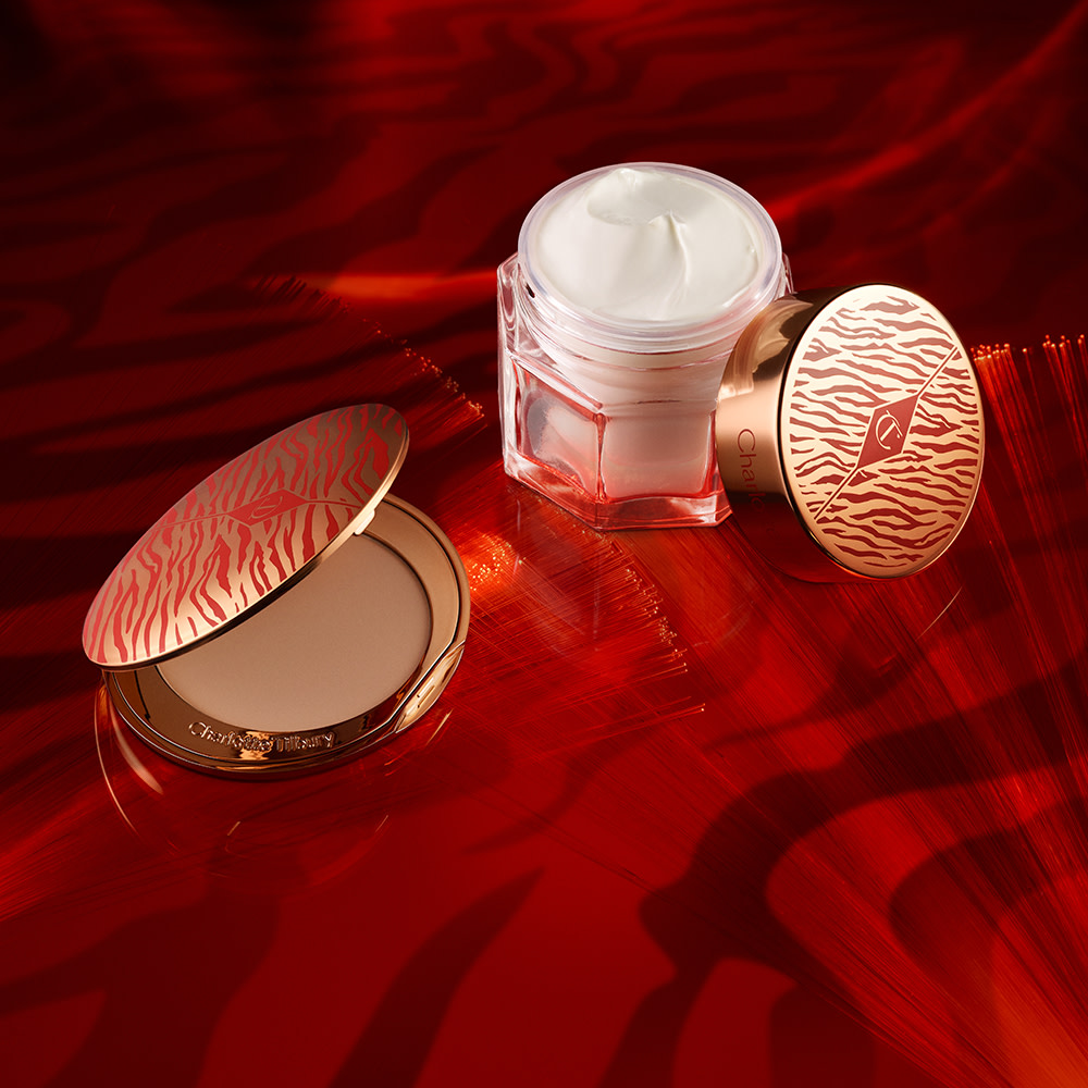 An open jar of face cream next to an open pressed powder compact, both with gold-coloured lids with red tiger stripes pattern on the lids for the Lunar New Year.