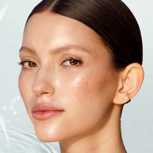 A light-tone brunette model wearing subtle eye makeup and rose-tinted lip balm with nothing else, displaying glowy, fresh skin, free from makeup.