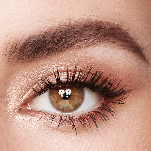 Single-eye close-up of a fair-tone model with hazel eyes wearing shimmery champagne, light brown, and rose gold eye makeup with jet-black lengthening mascara.