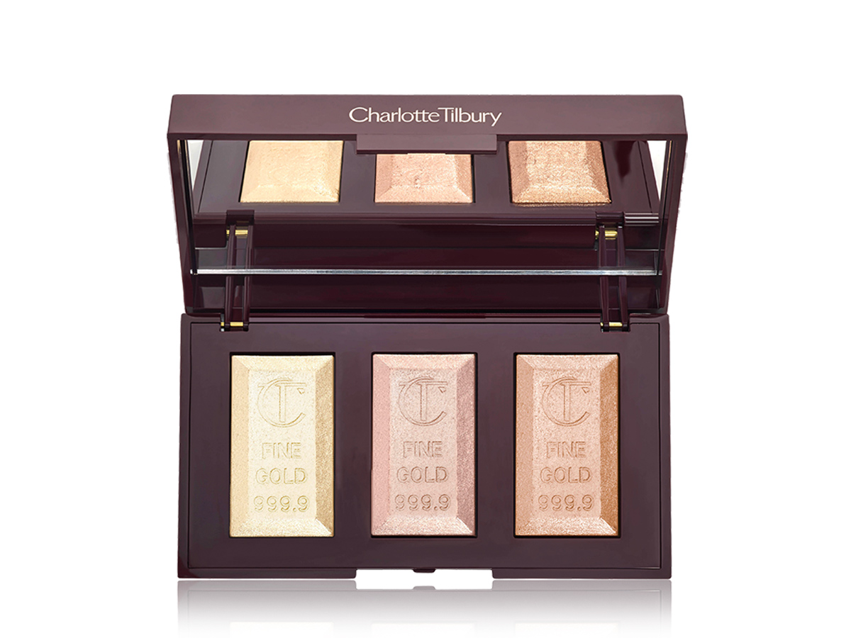 An open, mirrored-lid highlighter palette with three powder highlighters in shades of white gold, rose gold, and golden. 