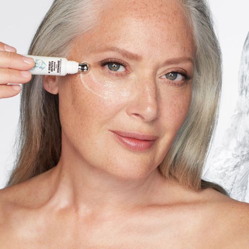 Fair-tone model with flawless, poreless, and glowy mature skin applying a white-coloured eye serum under her eyes that delivers a cooling sensation and moisturises. 