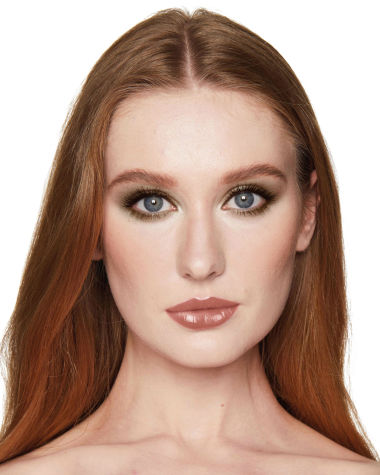 A fair-tone model with blue eyes wearing smokey green eye makeup with black eyeliner, soft brown blush, and nude brown lipstick. 