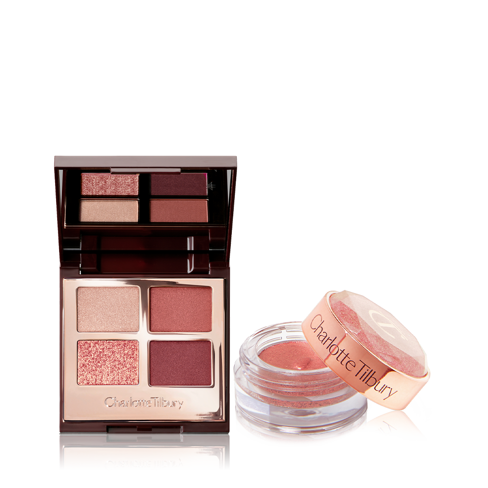 An open, mirrored-lid quad eyeshadow palette in berry-pink, red, and gold shades with a shimmery, cream eyeshadow in a berry-pink shade in a glass pot with its lid removed.