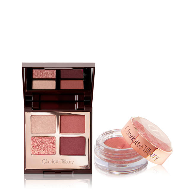 An open, mirrored-lid quad eyeshadow palette in berry-pink, red, and gold shades with a shimmery, cream eyeshadow in a berry-pink shade in a glass pot with its lid removed.