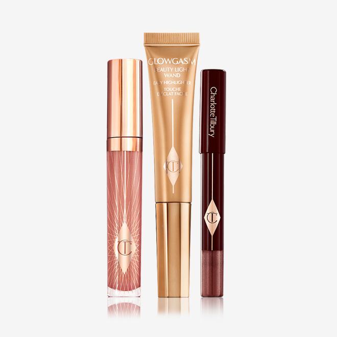 Glowing Eye, Lip and Cheek Kit closed Nude pink lip gloss in a glass tube with gold-coloured lid, a highlighter wand in a gold-colour, and a chubby eyeshadow stick in an amber-brown shade.