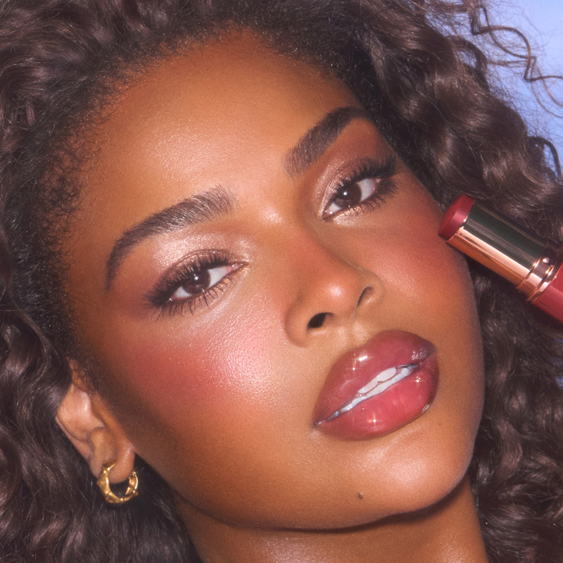 Model wears Unreal Blush Healthy Glow Stick in Cherry Glow
