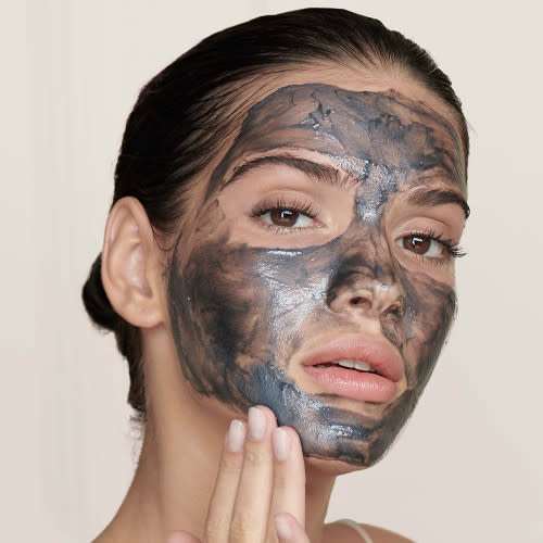 A light-tone brunette model applying a charcoal cleanser on her face.