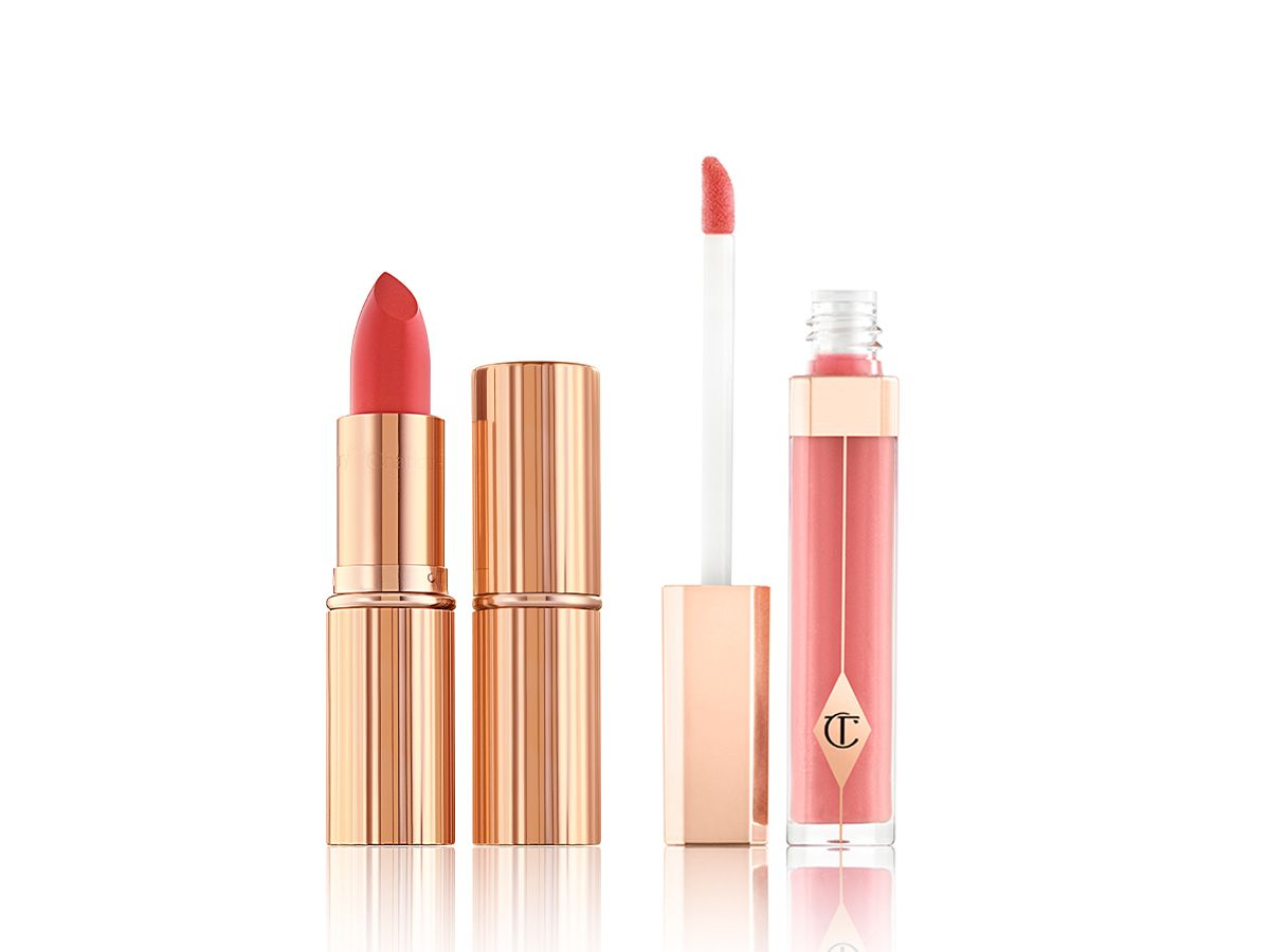Two lipsticks, with and without lid in a dark coral shade with a warm nude pink lip gloss with its doe-foot applicator next to it. 