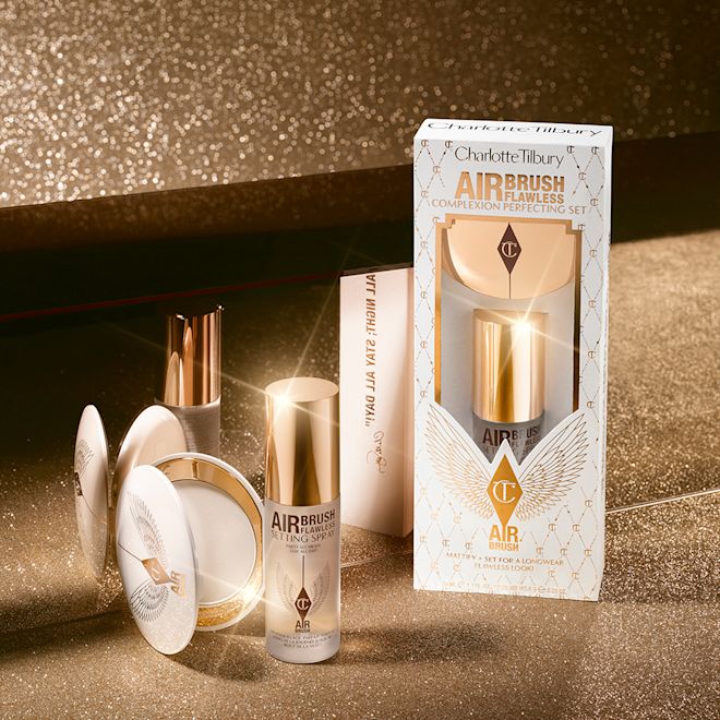 Airbrush Flawless Complexion Perfecting Set with box displayed Setting spray in a clear bottle with a gold-coloured lid with a setting powder compact in gold-packaging with a mirrored-lid along with a white and pink-coloured packaging box.