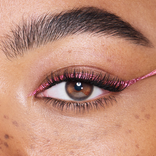 Single-eye close-up of a light-tone model with brown eyes wearing a glittery vivid, rose pink eyeliner.