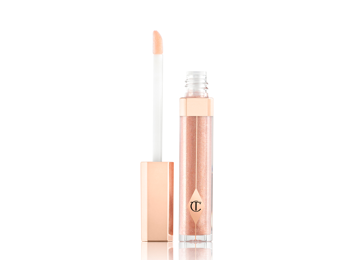 Sheer, shimmery lip gloss in a light golden shade in a glass tube with its doe-foot applicator next to it.