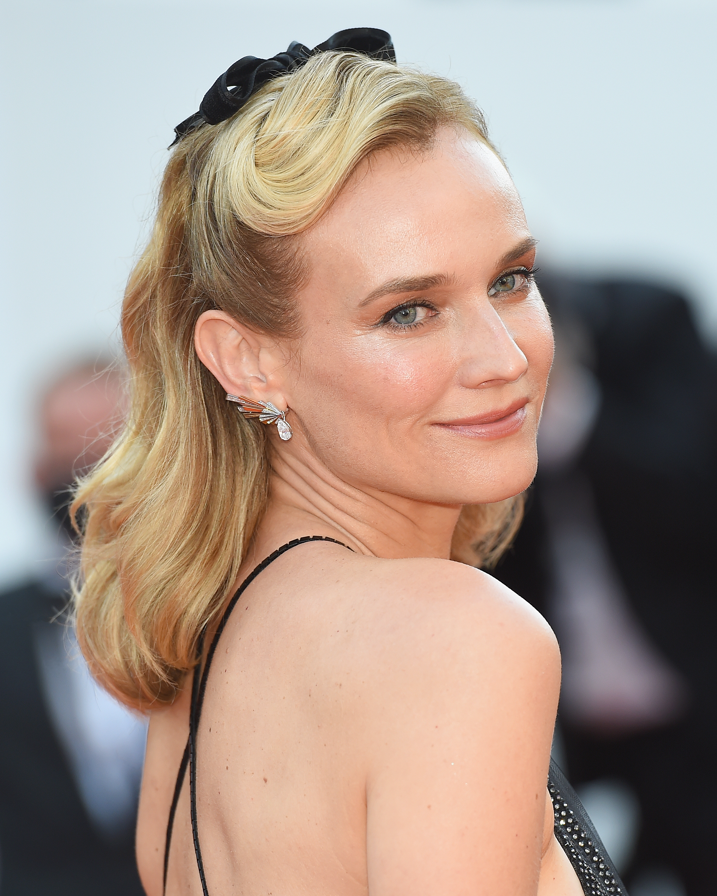Diane Kruger at Cannes Film Festival 2021, wearing a black gown with thin straps with shimmery silver earrings, and soft, glowy nude makeup done using Charlotte Tilbury products.